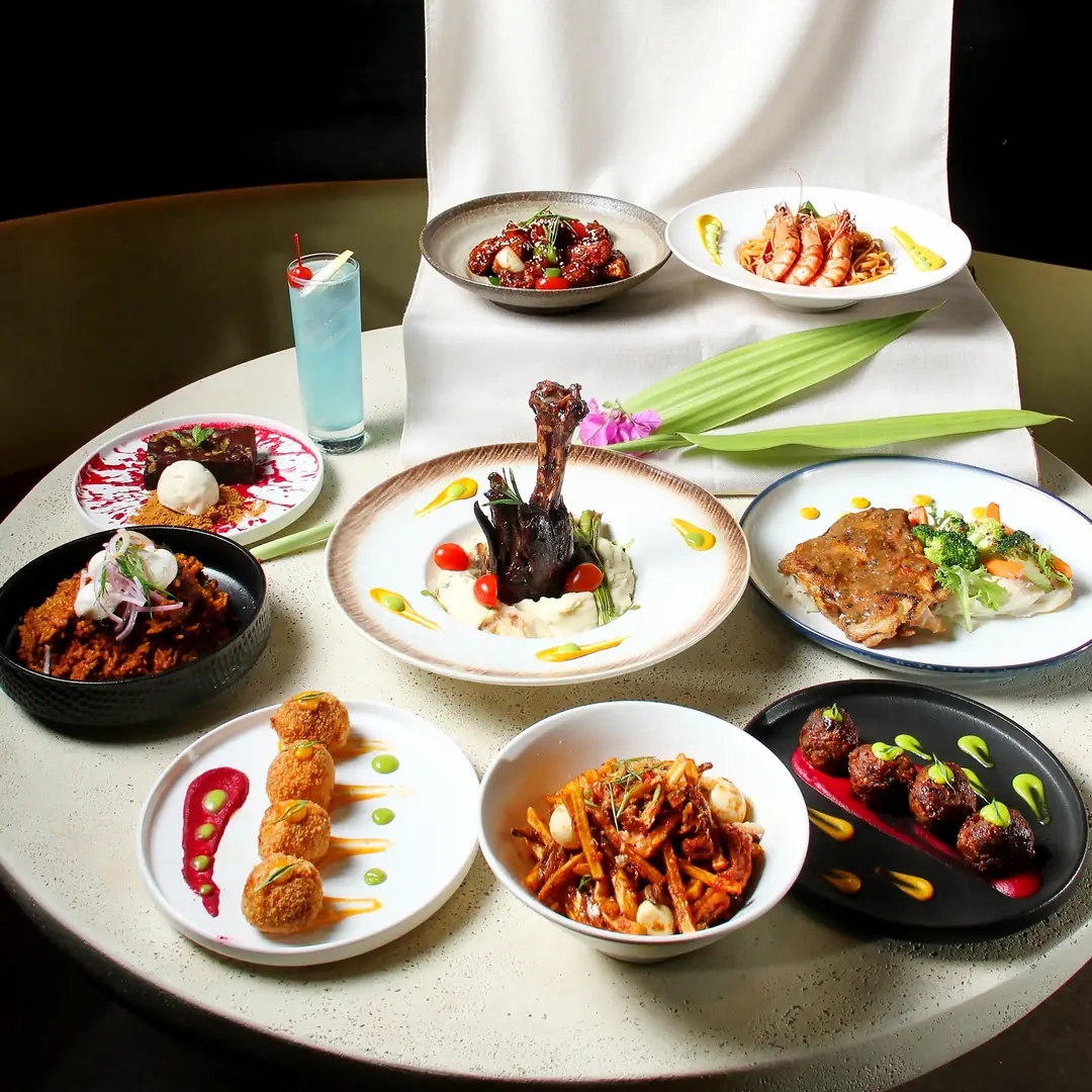 A spread of plated dishes from the Alfresco by Destino menu on a round table, including prawn linguine, fried bites and spiced meatballs